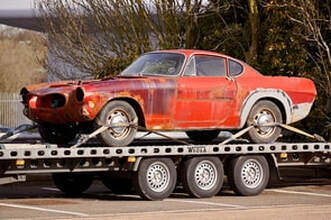 A red old classic Shelby auto on a flat bed.