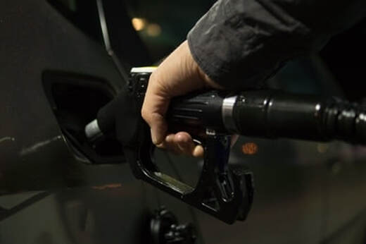 A hand pumping gas into a cars fuel tank.